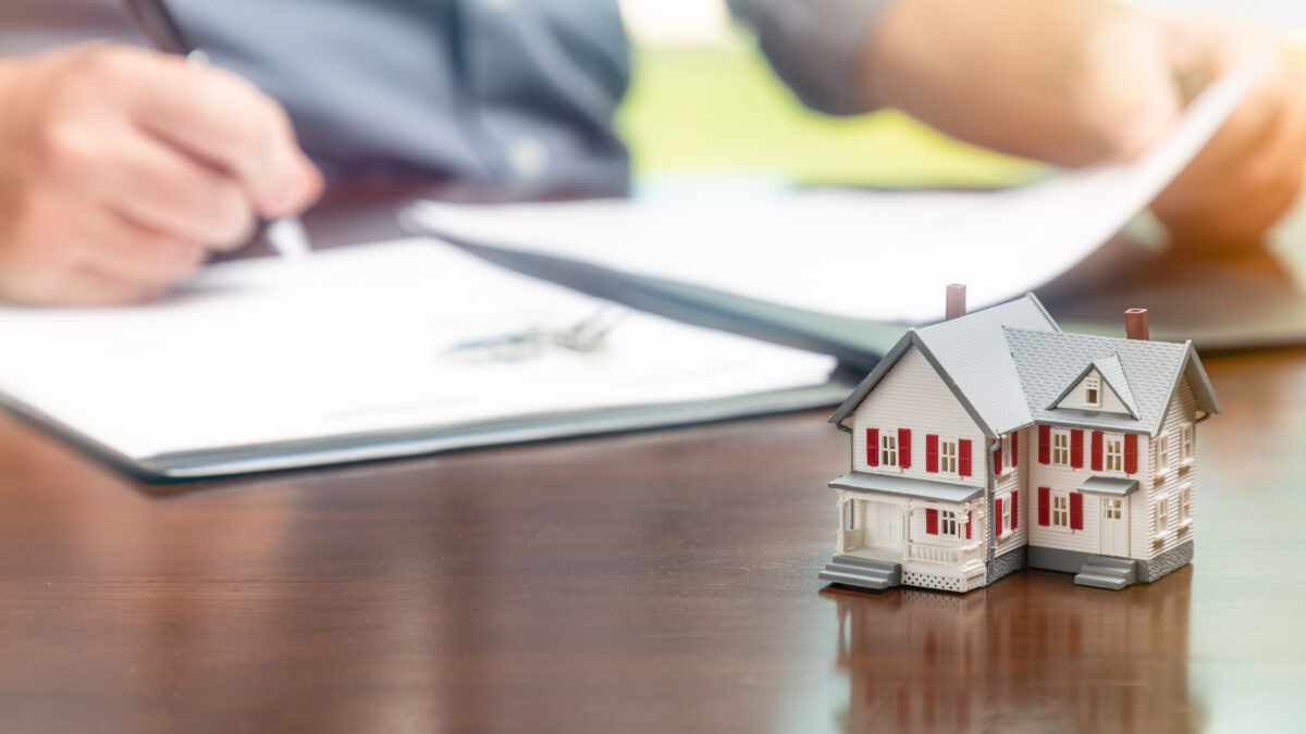 Man signing real estate contract papers with small model home in front.