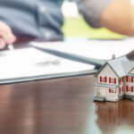 Man signing real estate contract papers with small model home in front.