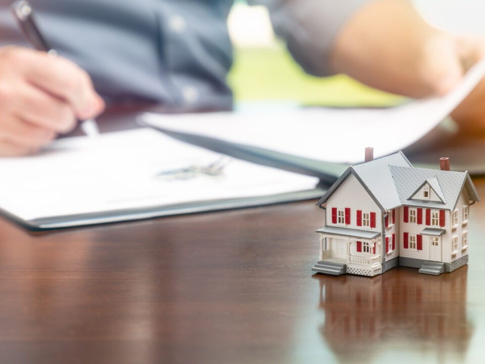 Man signing real estate contract papers with small model home in front.