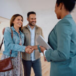 Happy woman shaking hands with real estate agent while buying new home with her husband.