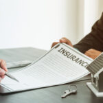 a hand holding a pen to sign an insurance form